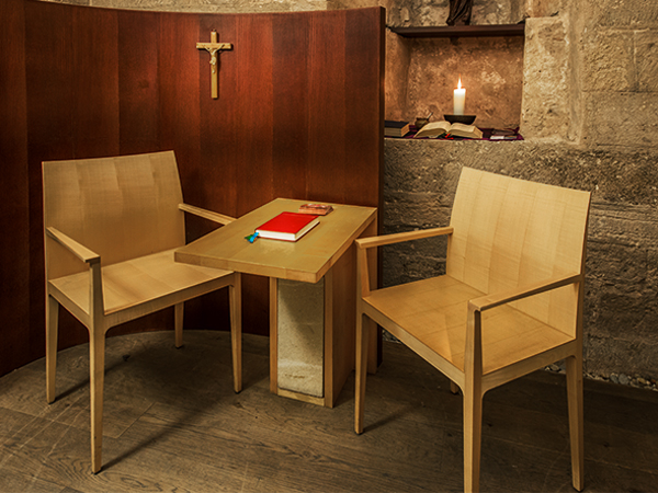 Confessional room with chairs, table, holy cross, candle, and red book